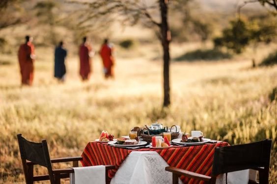 A table laid for dinner in the bush with Maasai walking past in the background