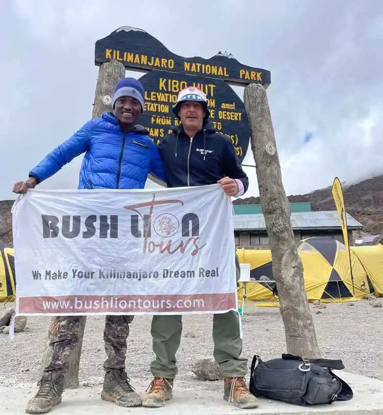 Kilimanjaro climbers at summit celebrating with Bush Lion Tours banner